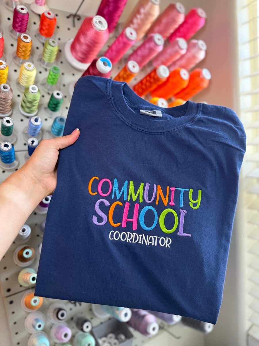 Navy tee with colorful Community School Coordinator embroidery