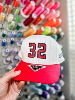 Red and white trucker hat with number 32 embroidery, held in front of a thread wall