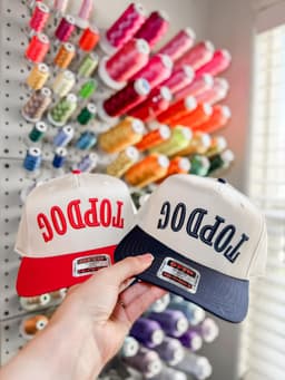 Two trucker hats with Top Dog embroidery, one red and one navy, held in front of a thread wall