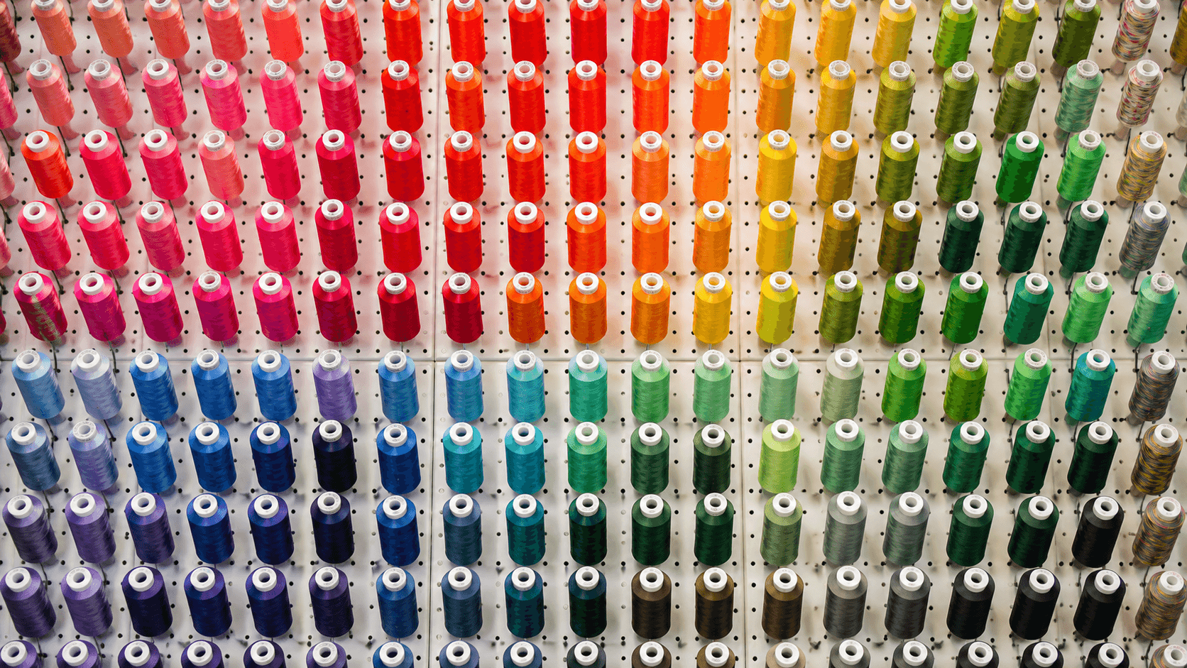 A full wall of colorful embroidery thread cones arranged on a pegboard